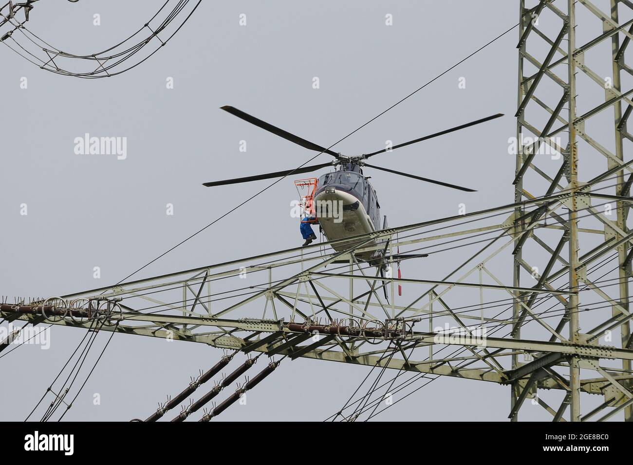Posizionamento di marcatori di protezione uccelli su una linea elettrica con l'aiuto di un elicottero e un fitter seduto al di fuori / Germania, Affoldern, 2017-04-10. Foto Stock