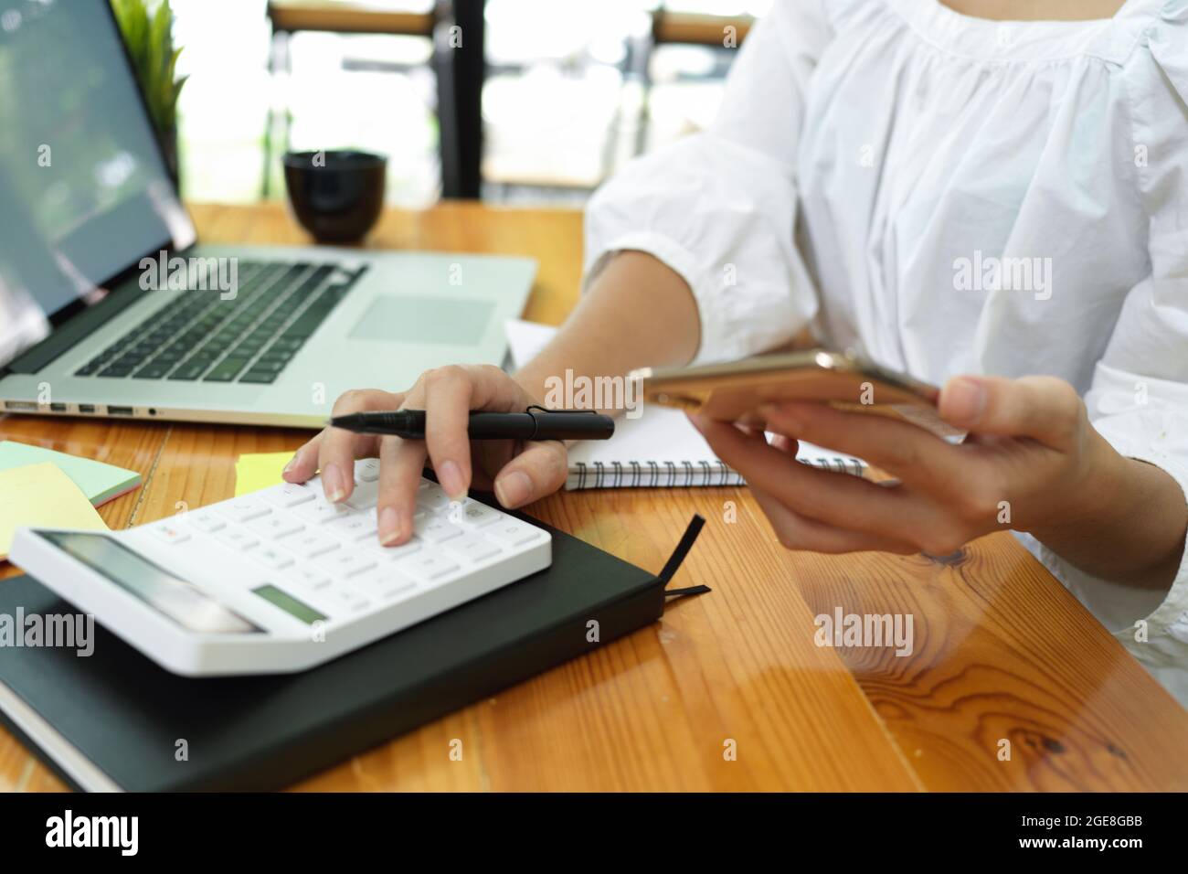 Donna d'affari che calcola i costi di marketing con calcolatrice, smartphone, computer portatile sulla scrivania Foto Stock