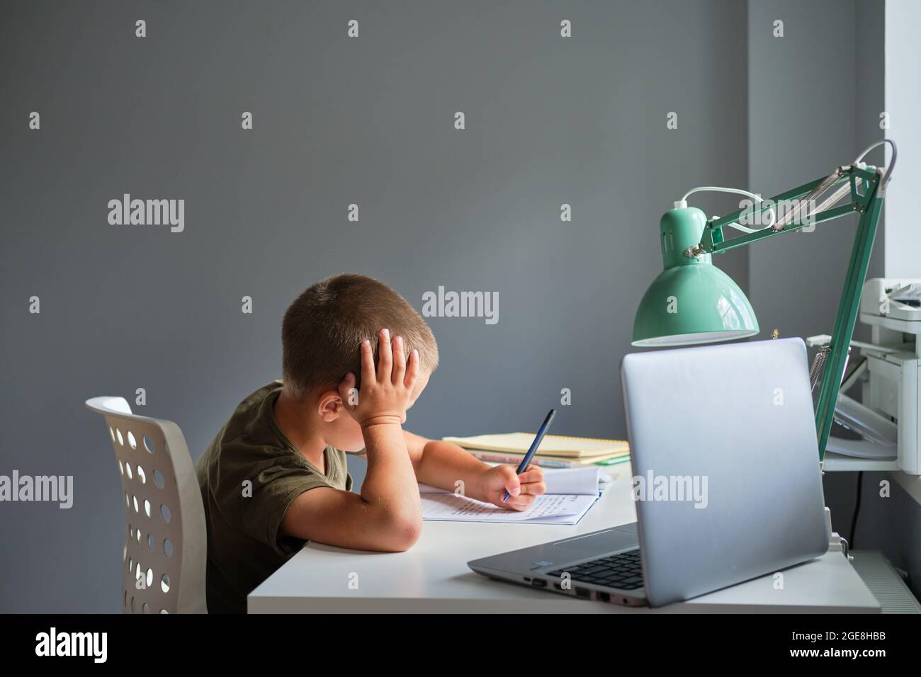 Lo scolaro seduto al tavolo e utilizzando il computer portatile mentre si lavora a casa. Concetto di homeschooling. Foto Stock