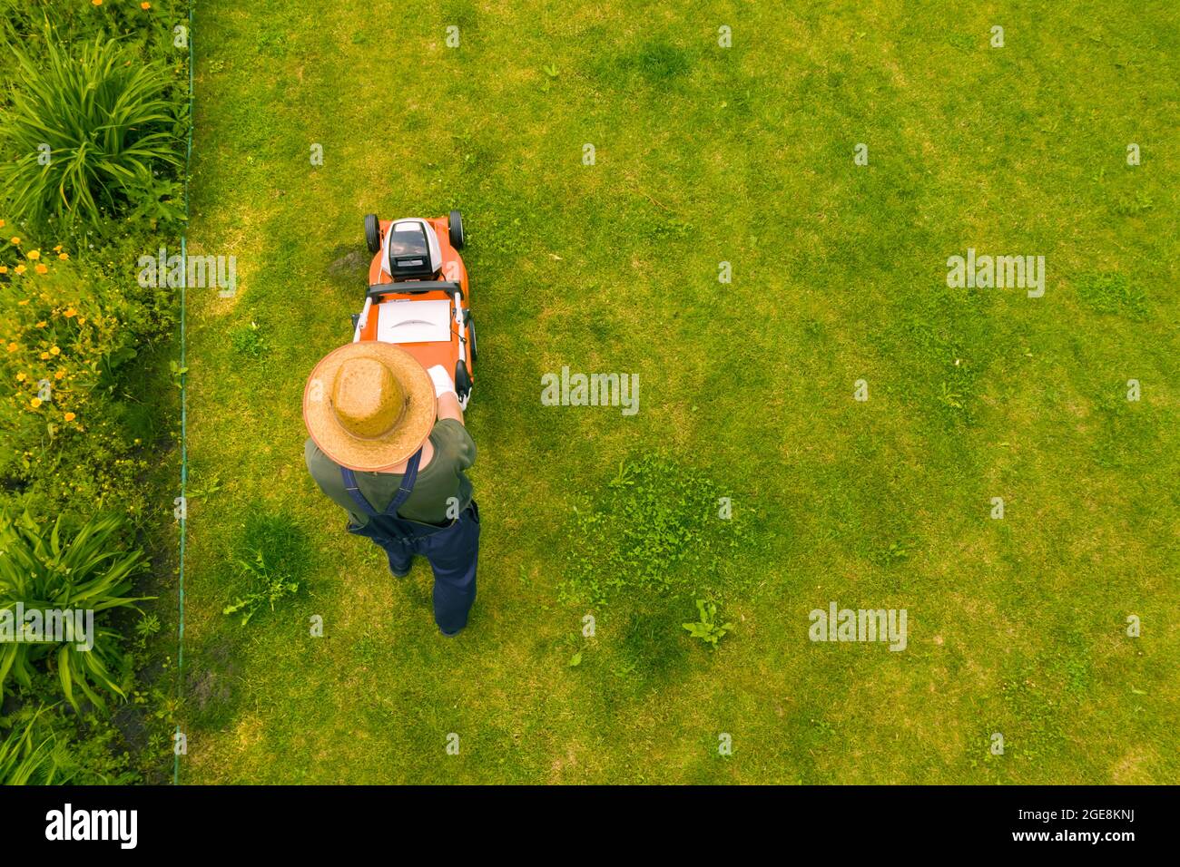 Un giovane sta falciando un prato con un tosaerba nel suo bel giardino verde Foto Stock