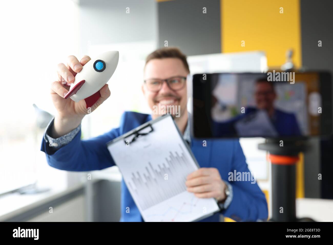 Maschio blogger tiene razzo e grafico con indicatori finanziari e registra video di formazione Foto Stock