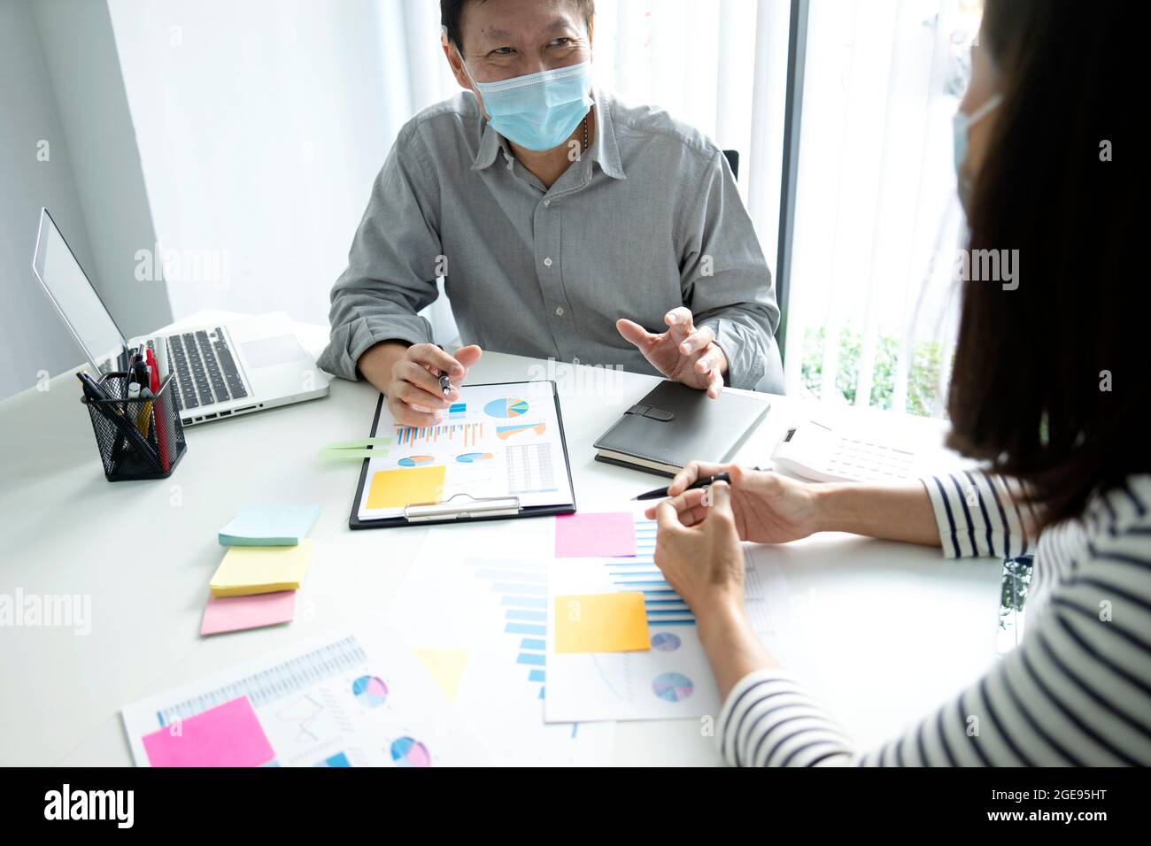 uomo d'affari che indossa una maschera che spiega circa l'operazione di marketing di affari ad un assistente o grafico del team del personale sul posto della nota del tavolo sulla parete i Foto Stock