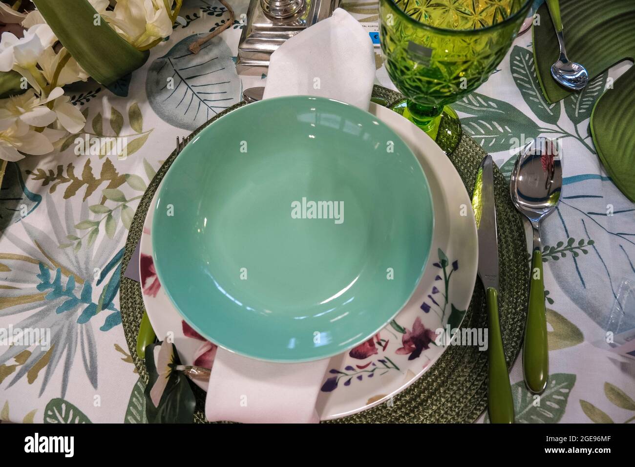 tavolo con piatti e posate su tovaglia floreale. ancora vita tavolo impostazione. Vaso con fiori Foto Stock