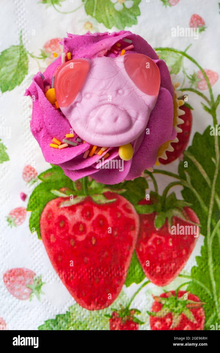 Torta Percy Pig party con cupcake di M&S, sita su tovagliolo con serviette di fragole d'estate Foto Stock