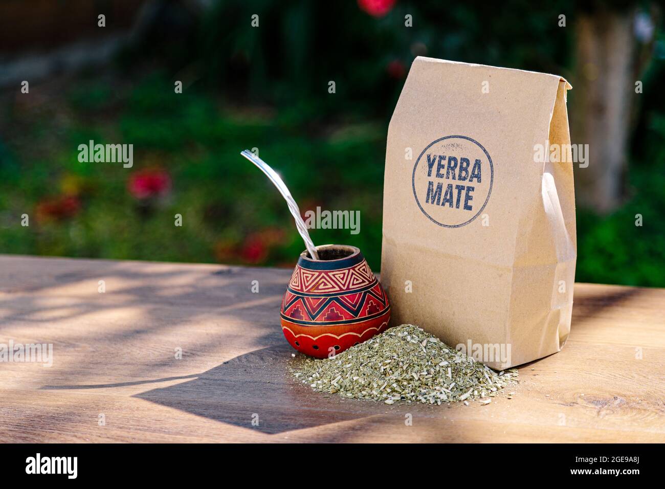 Una confezione rustica di carta marrone con un tradizionale compagno di calabasci su un tavolo di legno con yerba mate sparso su di esso. Foto Stock