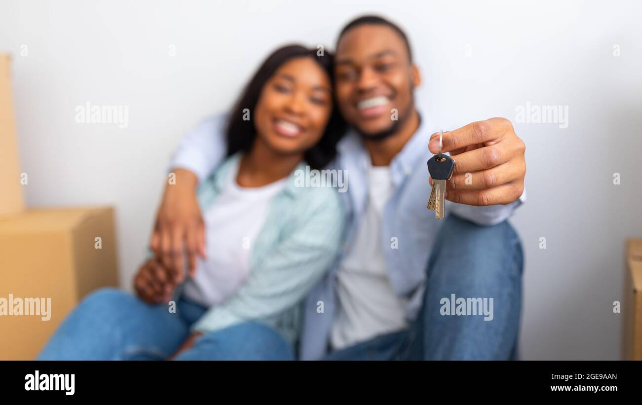 Nuova casa. Eccitati sposi neri che mostrano le chiavi, seduti nella loro casa dopo il trasferimento, concentrarsi sulla chiave, panorama Foto Stock