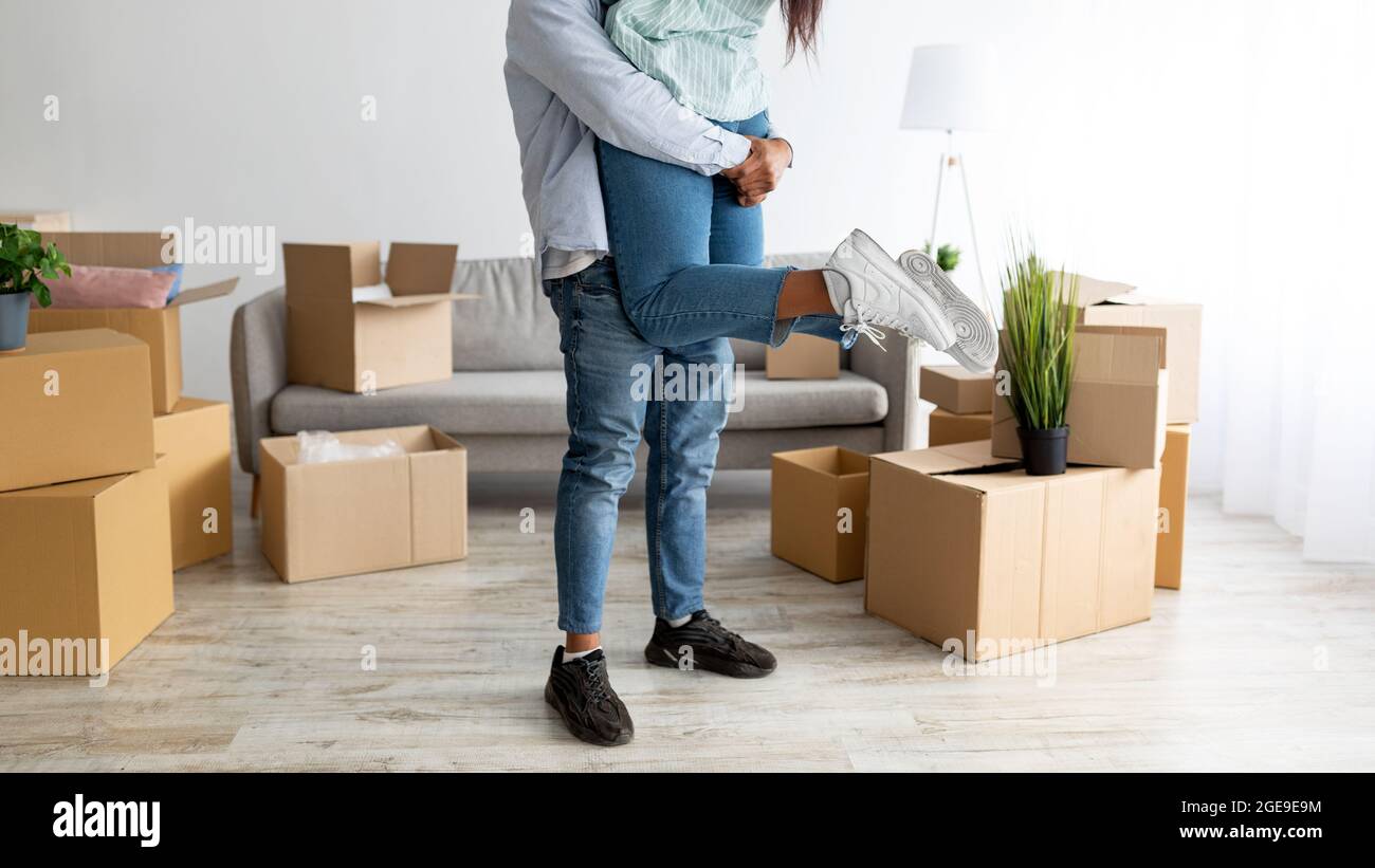 Spostarsi in casa propria. Amore marito nero sollevare sua moglie e divertirsi tra le scatole in nuovo appartamento, raccolto Foto Stock