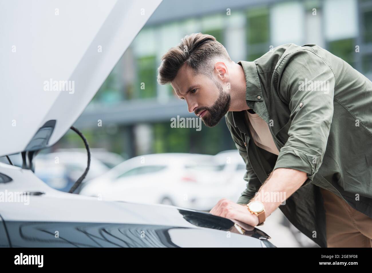 Vista laterale di un uomo concentrato che guarda l'auto con cofano aperto Foto Stock