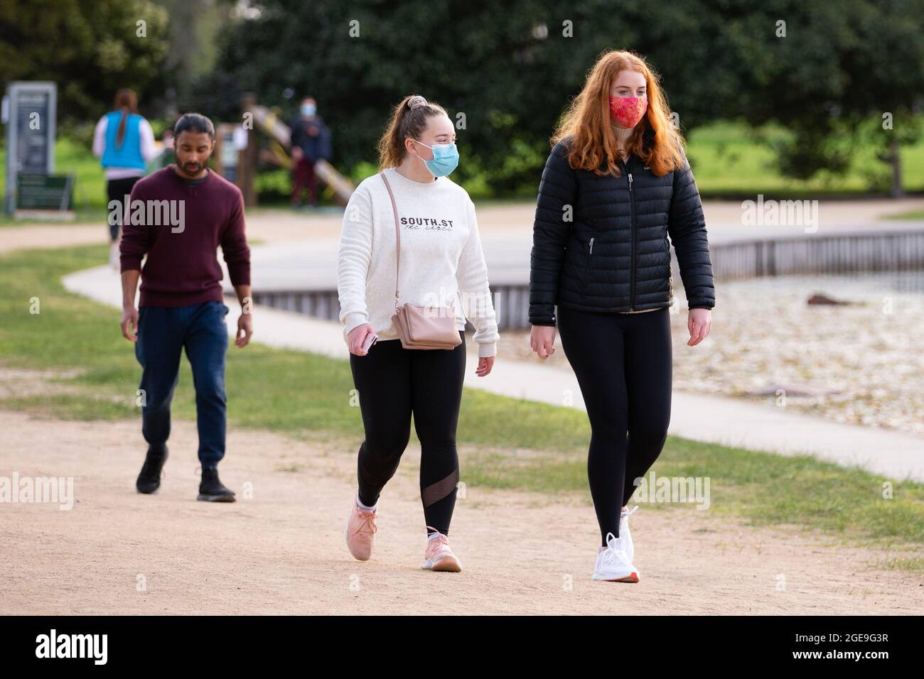 Melbourne, Australia, 18 agosto 2021. Due ragazze in maschere di faccia sono viste camminare lungo il lago di Albert Park durante il secondo giorno di un marciapiede, parchi giochi chiusi, e un ritorno ai permessi di lavoro sotto un 6 ° blocco COVID continua a Melbourne. Credit: Dave Hewison/Speed Media/Alamy Live News Foto Stock