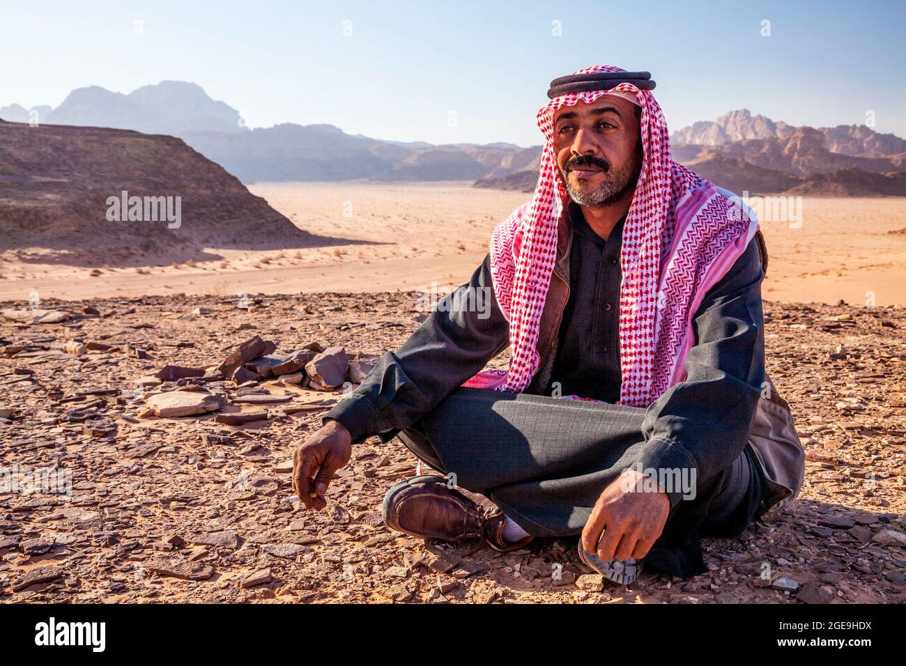 Un beduino uomo si siede sullo sfondo del deserto giordano a Wadi Rum o a valle della luna Foto Stock