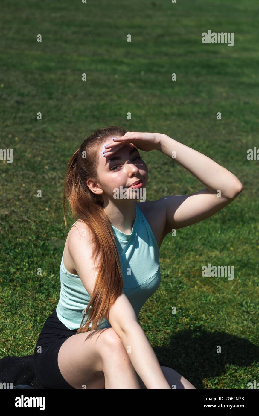 Giovane caucasica dai capelli lunghi in abbigliamento sportivo sta facendo yoga nel parco pubblico. Allenamento all'aperto. Lo yoga pone Foto Stock