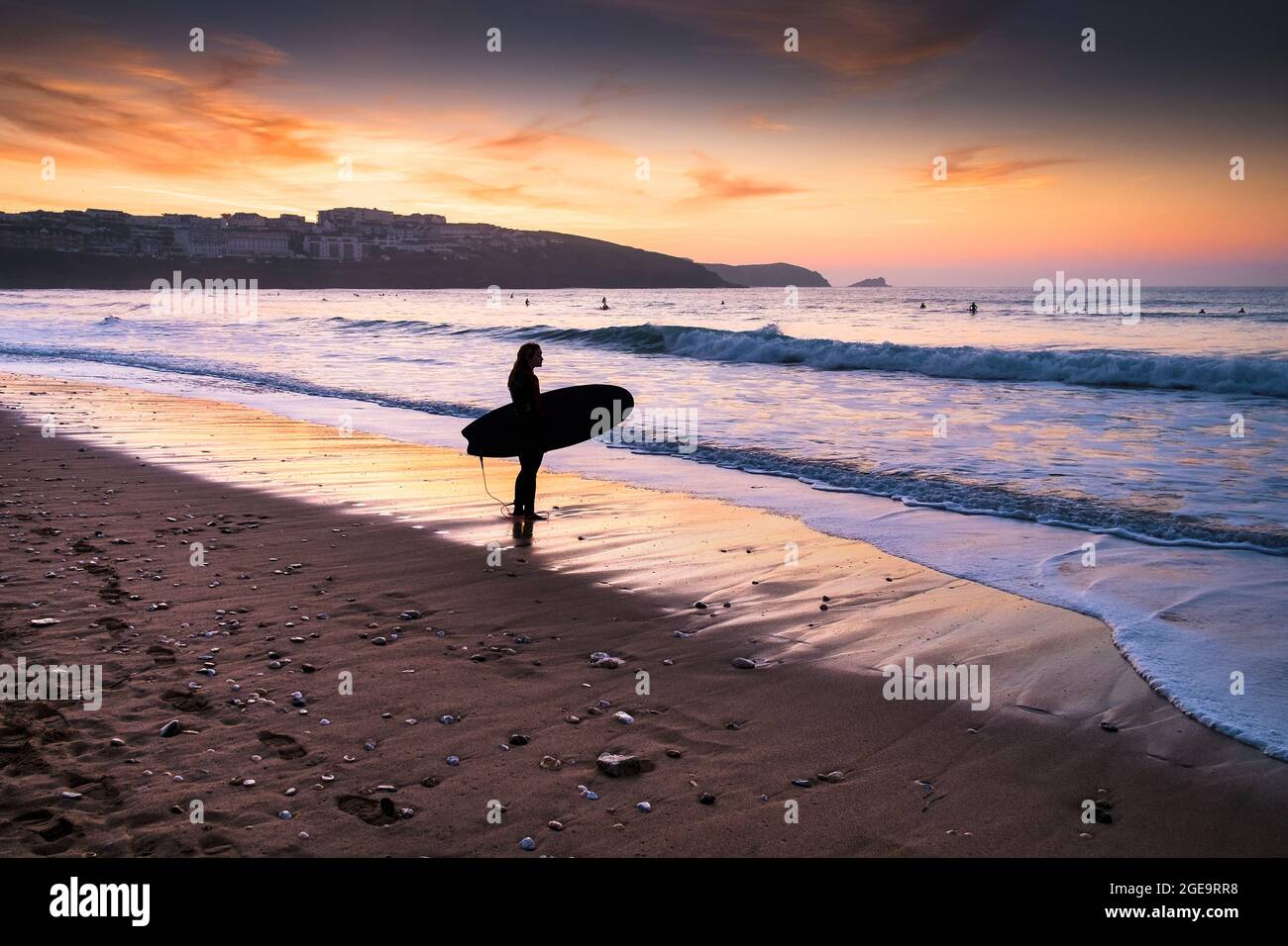 Un surfista che si erge sulla spiaggia di Fistral, silhouette del tramonto a Newquay in Cornovaglia. Foto Stock