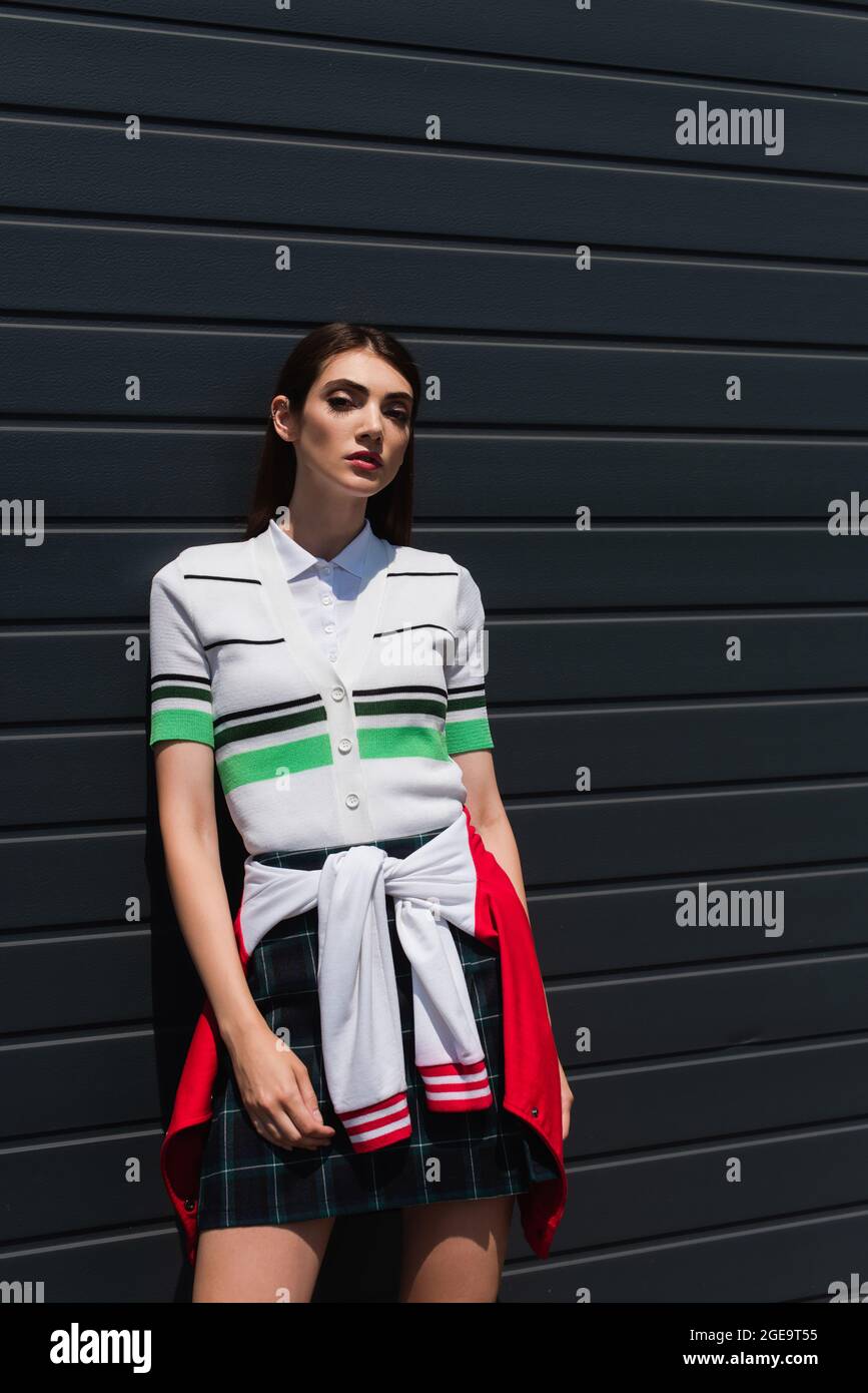 bella donna in polo a righe t-shirt guardando la fotocamera mentre si appoggia sulla parete grigia Foto Stock