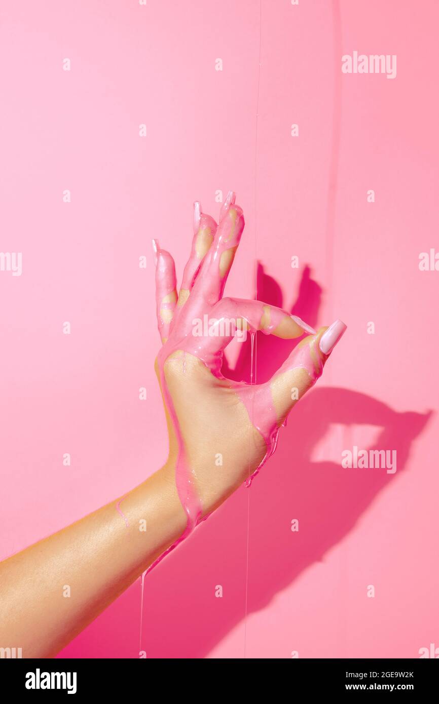 Crop Unriconoscibile Donna mostrando mano con manicure e fluidi di vernice brillante su sfondo rosa Foto Stock
