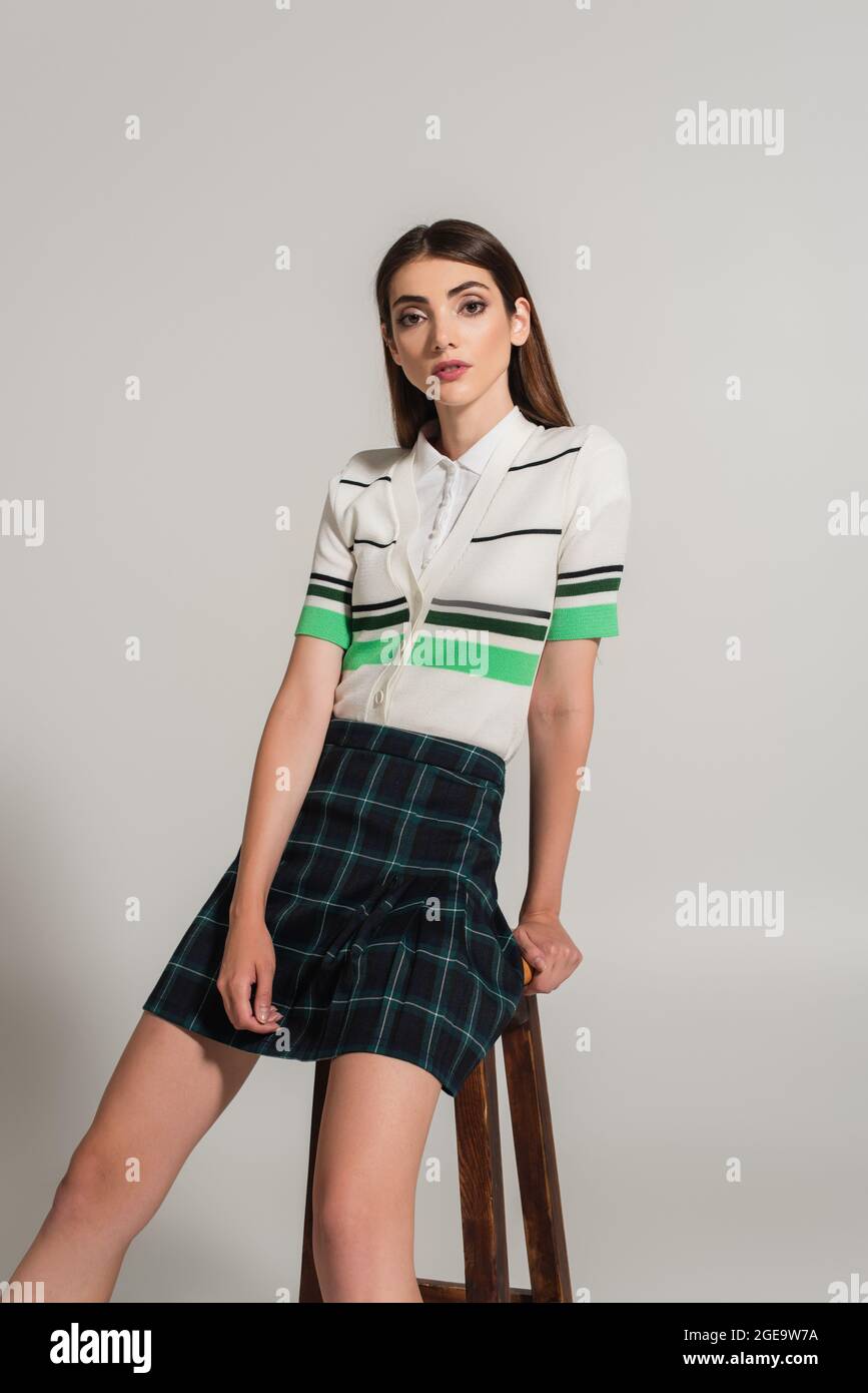 bella donna in polo a righe t-shirt e gonna plaid guardando la fotocamera su sfondo grigio Foto Stock