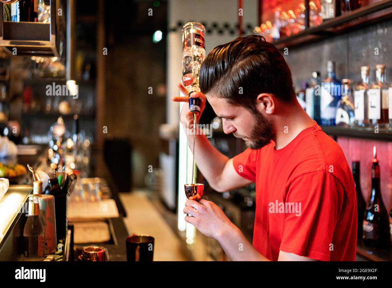 Vista laterale del barman concentrato che versa l'alcool da una bottiglia in un bicchiere di metallo mentre prepara il cocktail al bar Foto Stock