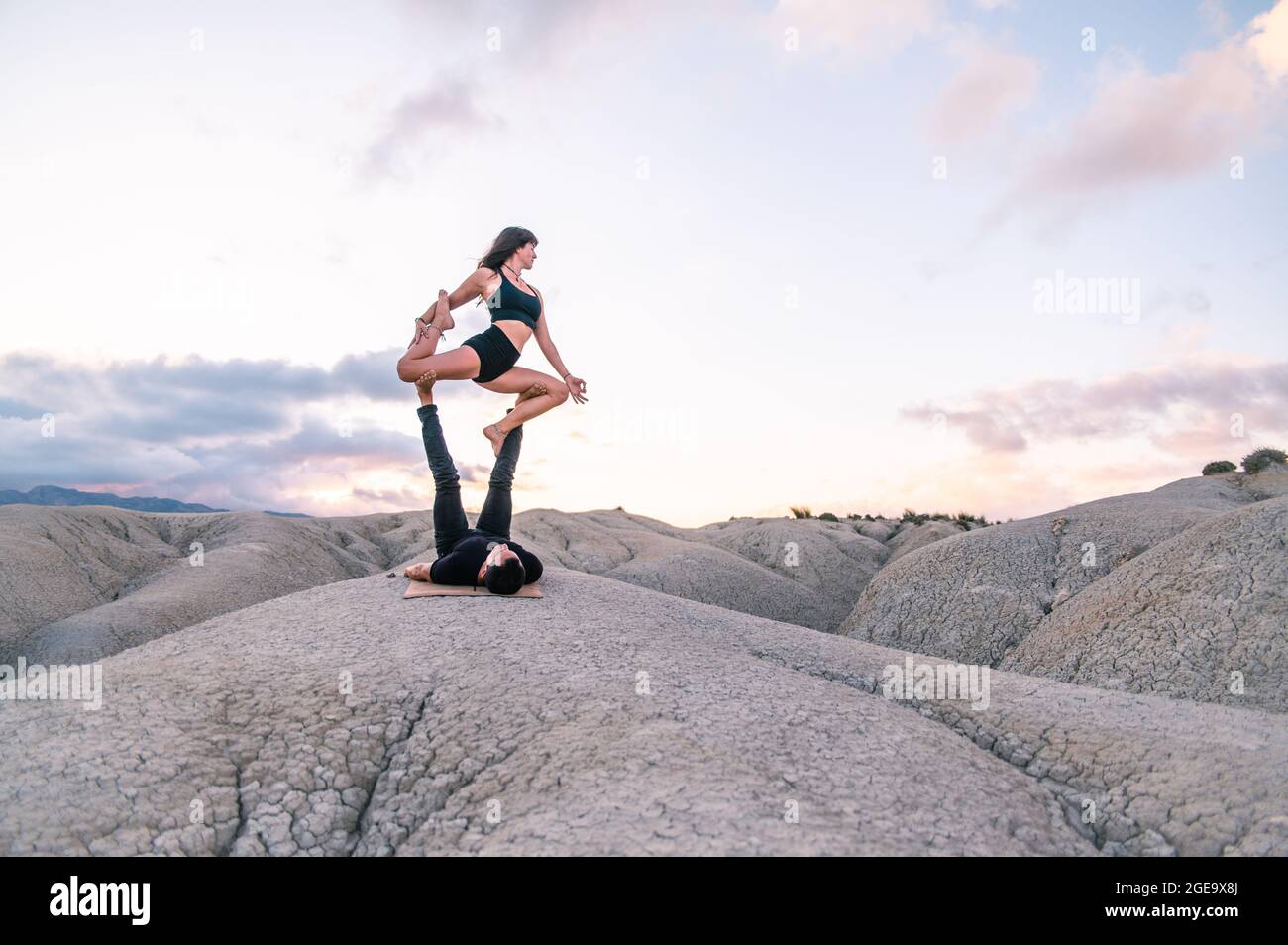 Donna serena equilibrio in re Pigeon posa sulle gambe dell'uomo mentre pratica acroyoga in altopiani Foto Stock