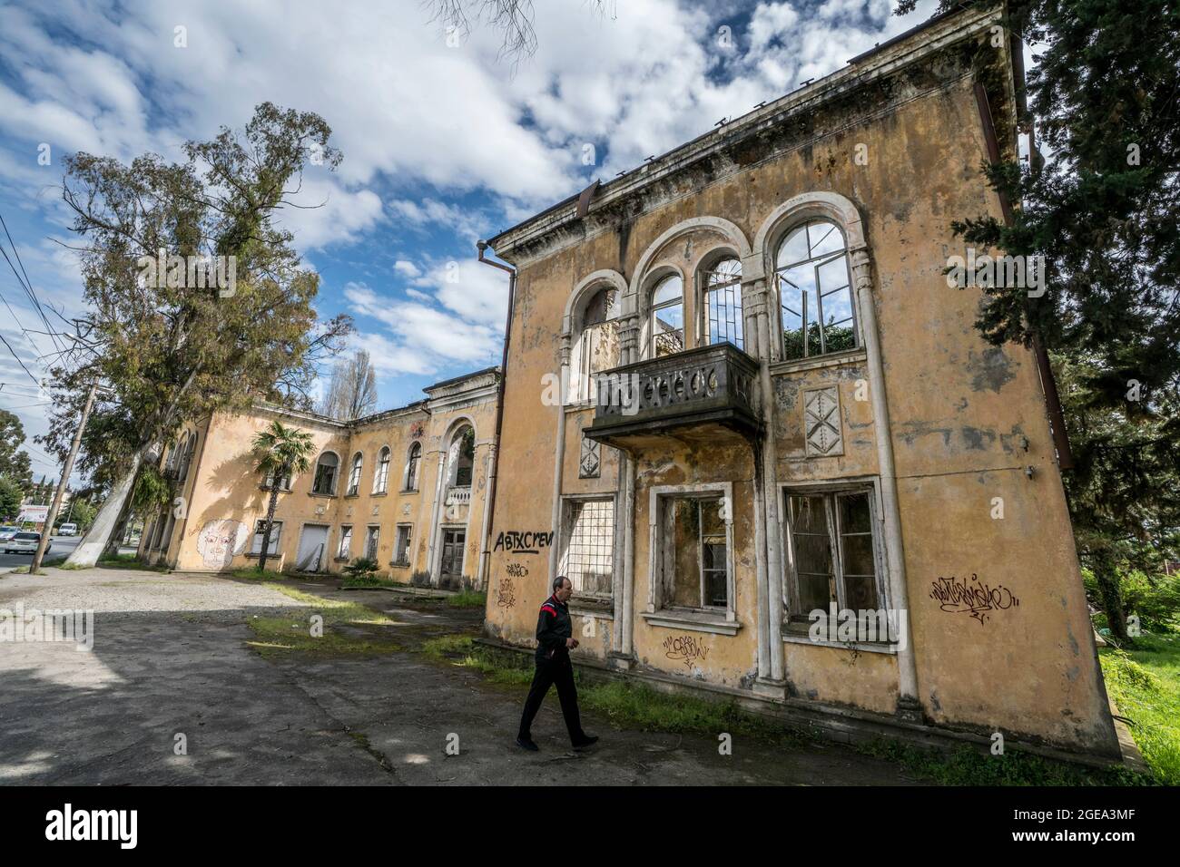 Un uomo passa davanti a un guscio rovinato e coperto di graffiti, che era un tempo un opulento palazzo prima che la guerra ha colpito la regione dell'Abkhazia. Foto Stock