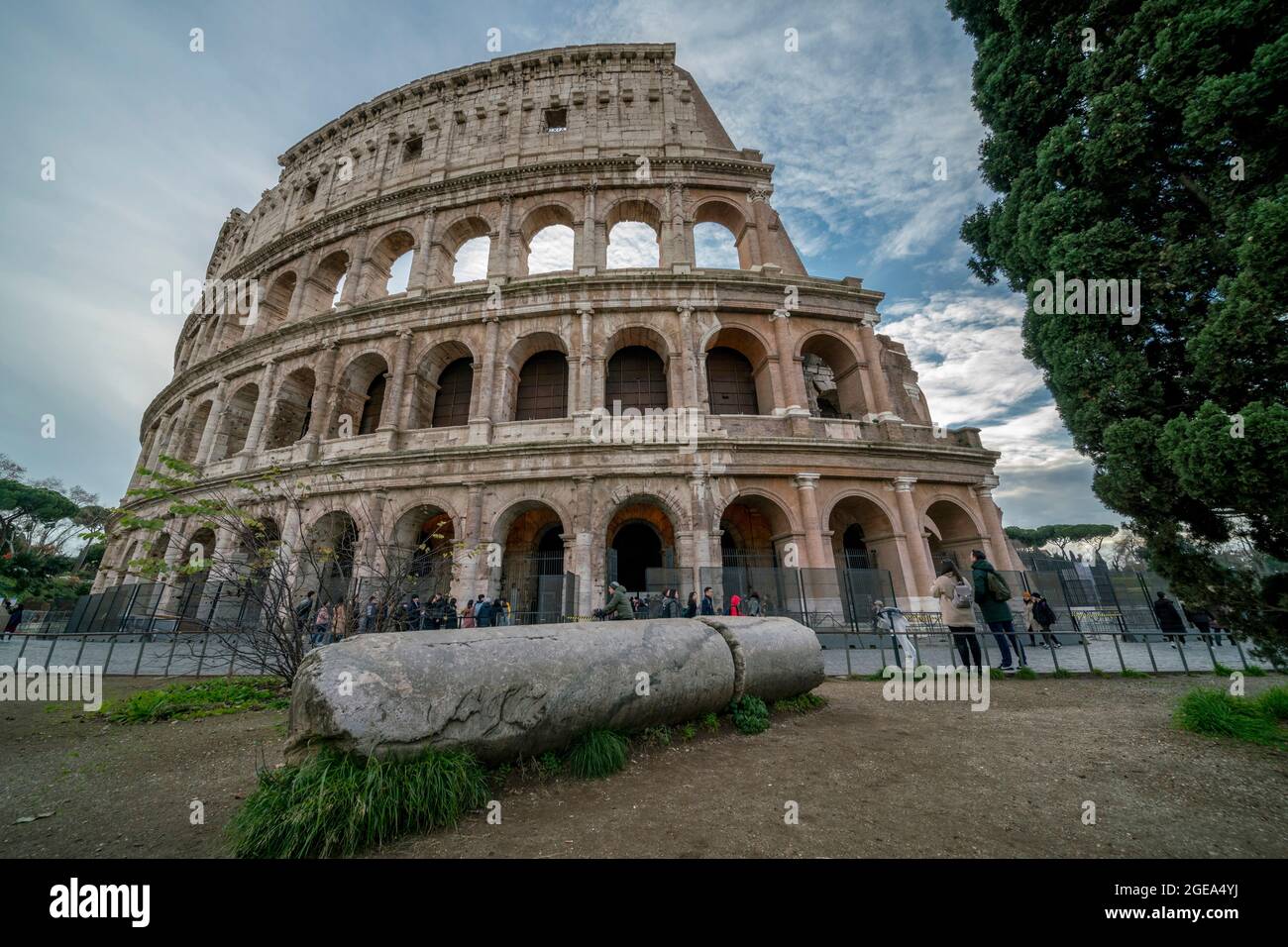 Una colonna caduta si trova sotto l'imponente Colosseo mentre i turisti guardano verso l'alto a Roma. Foto Stock