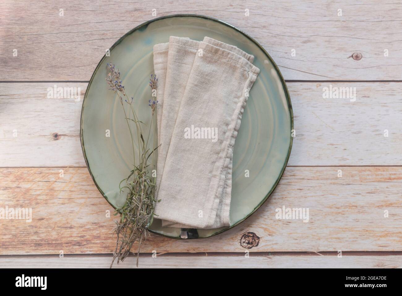 Piatto artigianale turchese, tovagliolo e ciuffi di lavanda essiccati su tavolo di legno. Vista dall'alto, spazio di copia, impostazione tabella. Sfondo per menu, layout. Foto Stock