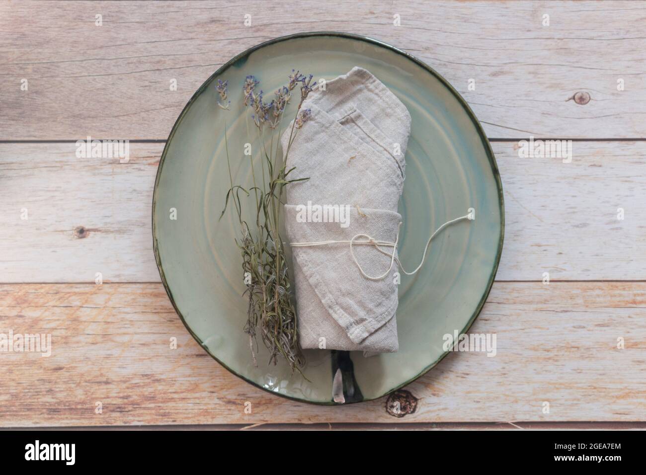 Piatto artigianale turchese, tovagliolo e ciuffi di lavanda essiccati su tavolo di legno. Vista dall'alto, spazio di copia, impostazione tabella. Sfondo per menu, layout. Foto Stock