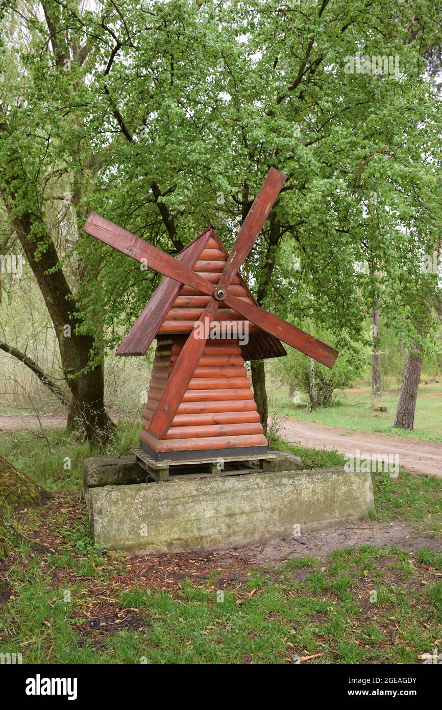 Un piccolo mulino marrone decorativo in legno si trova nel giardino sullo sfondo di alberi su un piedistallo in pietra Foto Stock