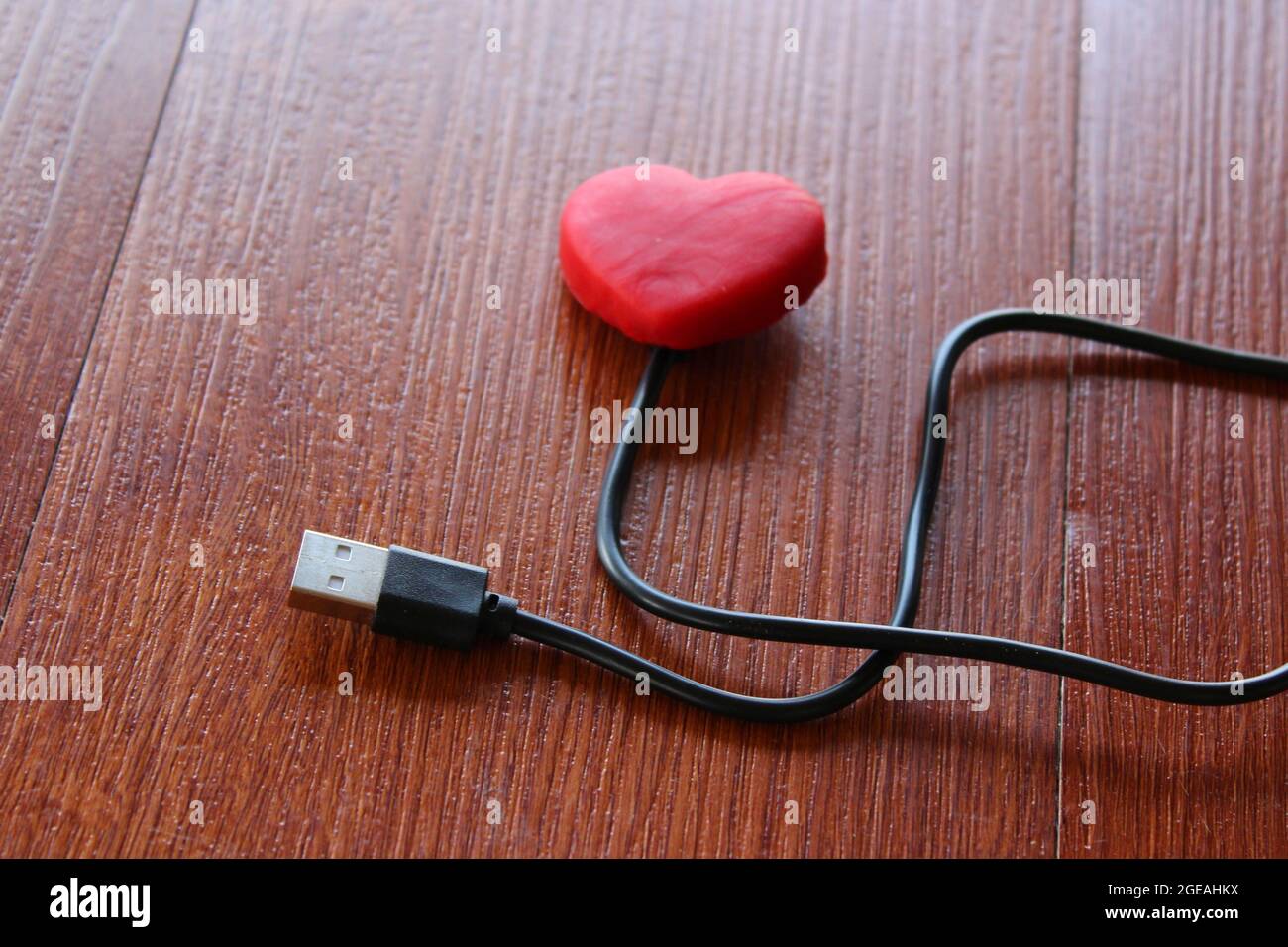 Cuore rosso con cavo usb su sfondo in legno. Amore e concetto di tecnologia Foto Stock