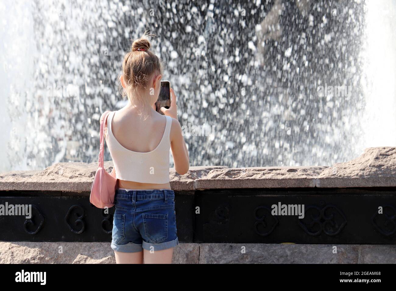 Foto della ragazza del capretto su smartphone fotocamera getti d'acqua della fontana. Bambini in estate, tempo caldo in città Foto Stock