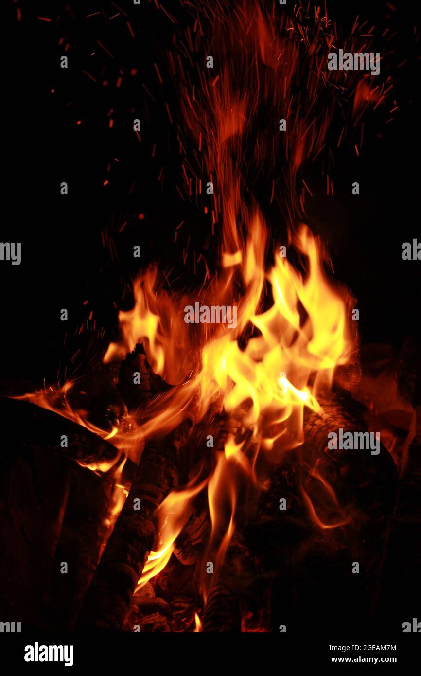 Un fuoco che brucia, tronchi di legno, scintille rosse e fiamme gialle su sfondo scuro Foto Stock