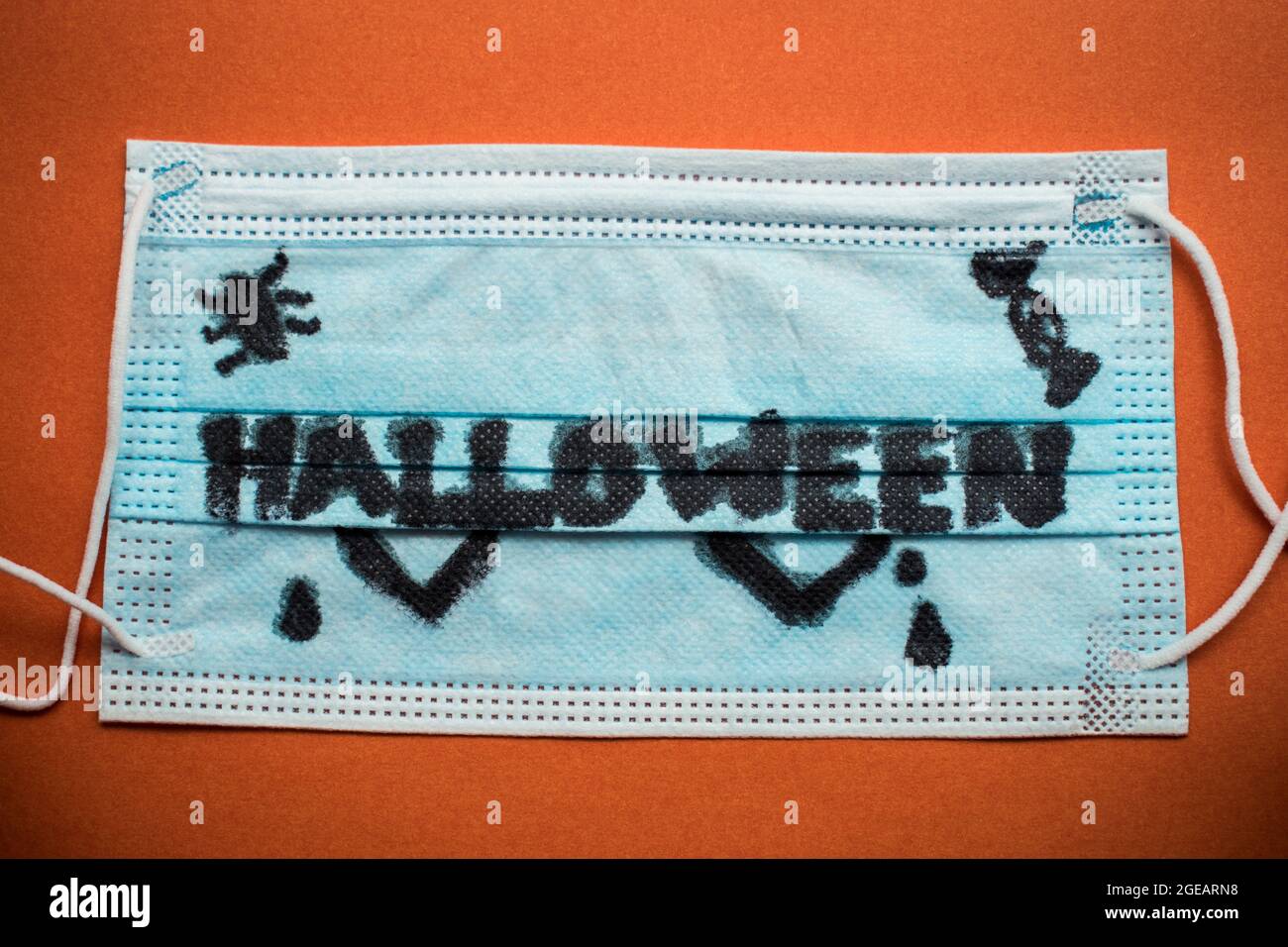 Parola di Halloween scritta su una maschera medica su una superficie arancione Foto Stock