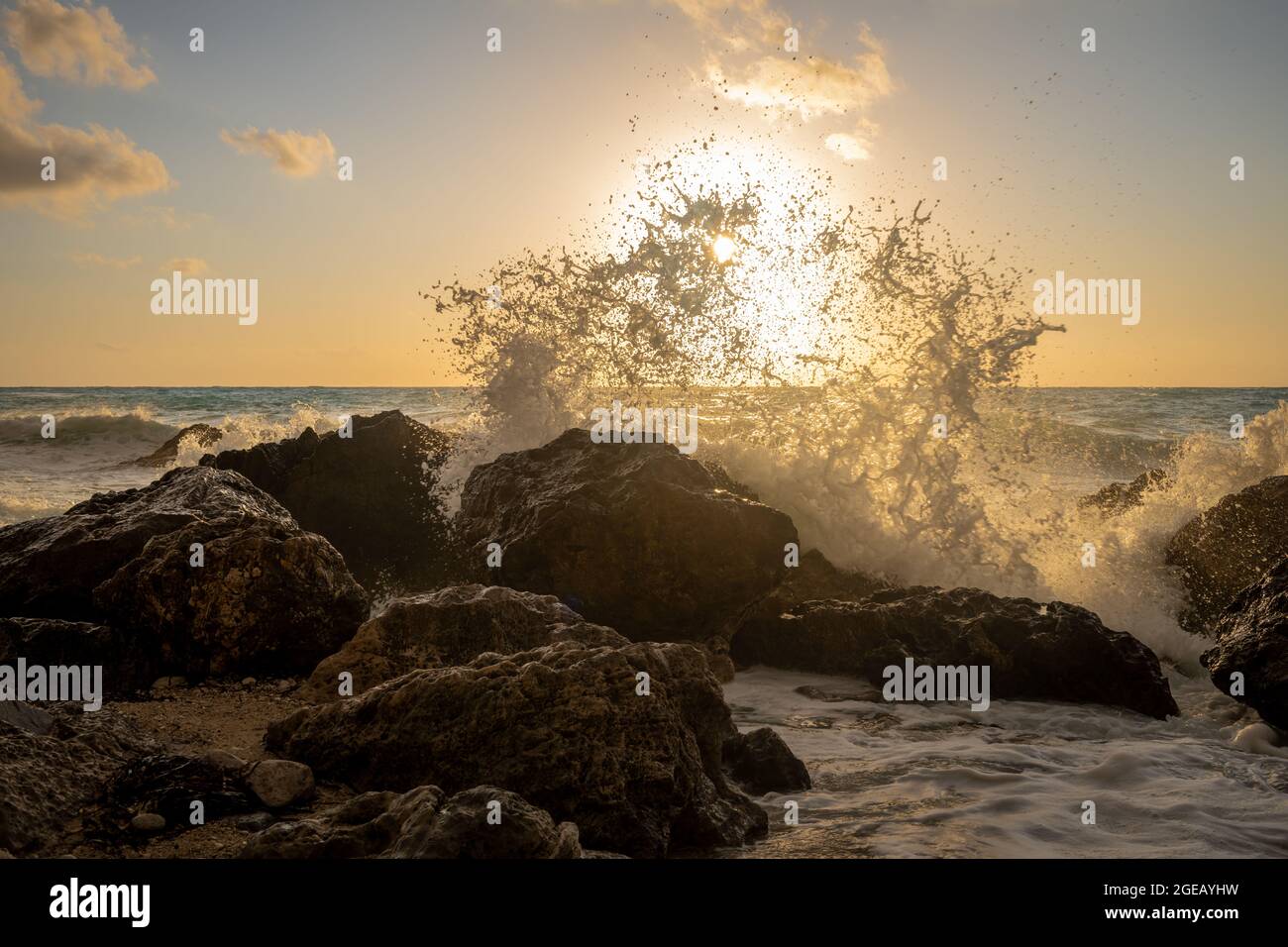 Onde che si infrangono sulle rocce della spiaggia con il sole che tramonta sotto l'orizzonte. Foto Stock