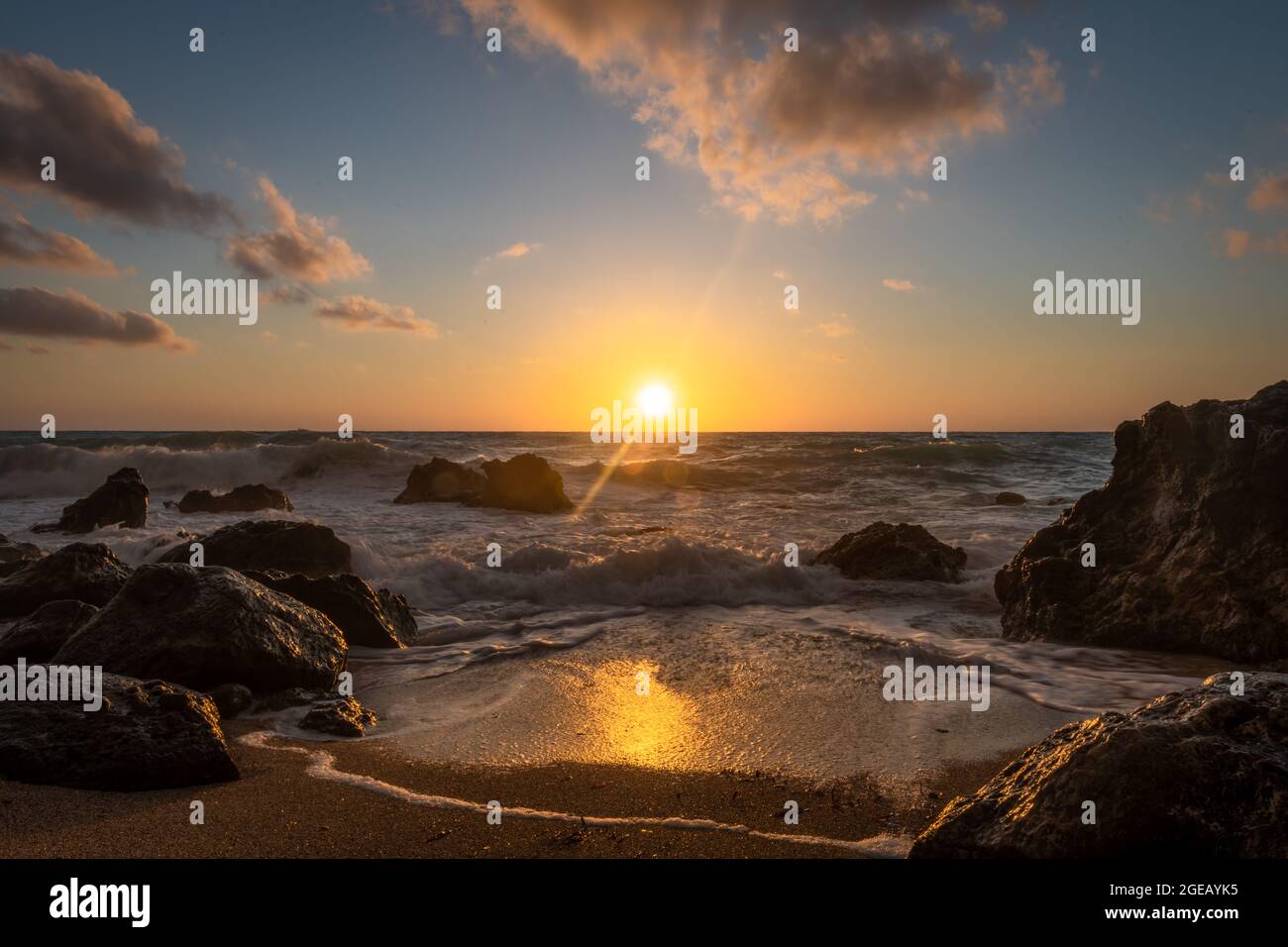 Un bel tramonto dorato con riflessi sulle onde che si lavano sulla spiaggia e il sole che tramonta dietro l'orizzonte. Foto Stock