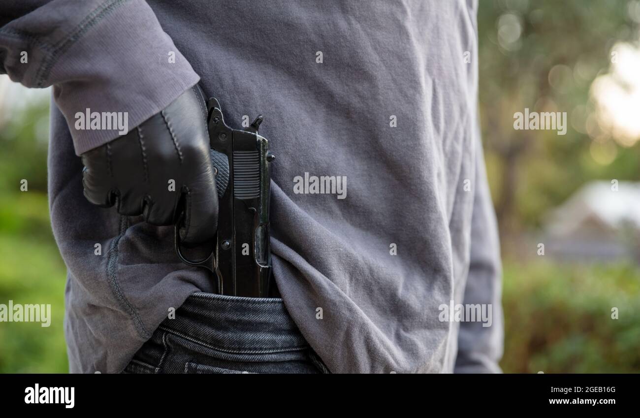 Un uomo armato che tira fuori una pistola con la sua mano guanto, sfoca lo sfondo della natura all'aperto. Pronto a sparare armi, minacce, violenza e pericolo concetto Foto Stock