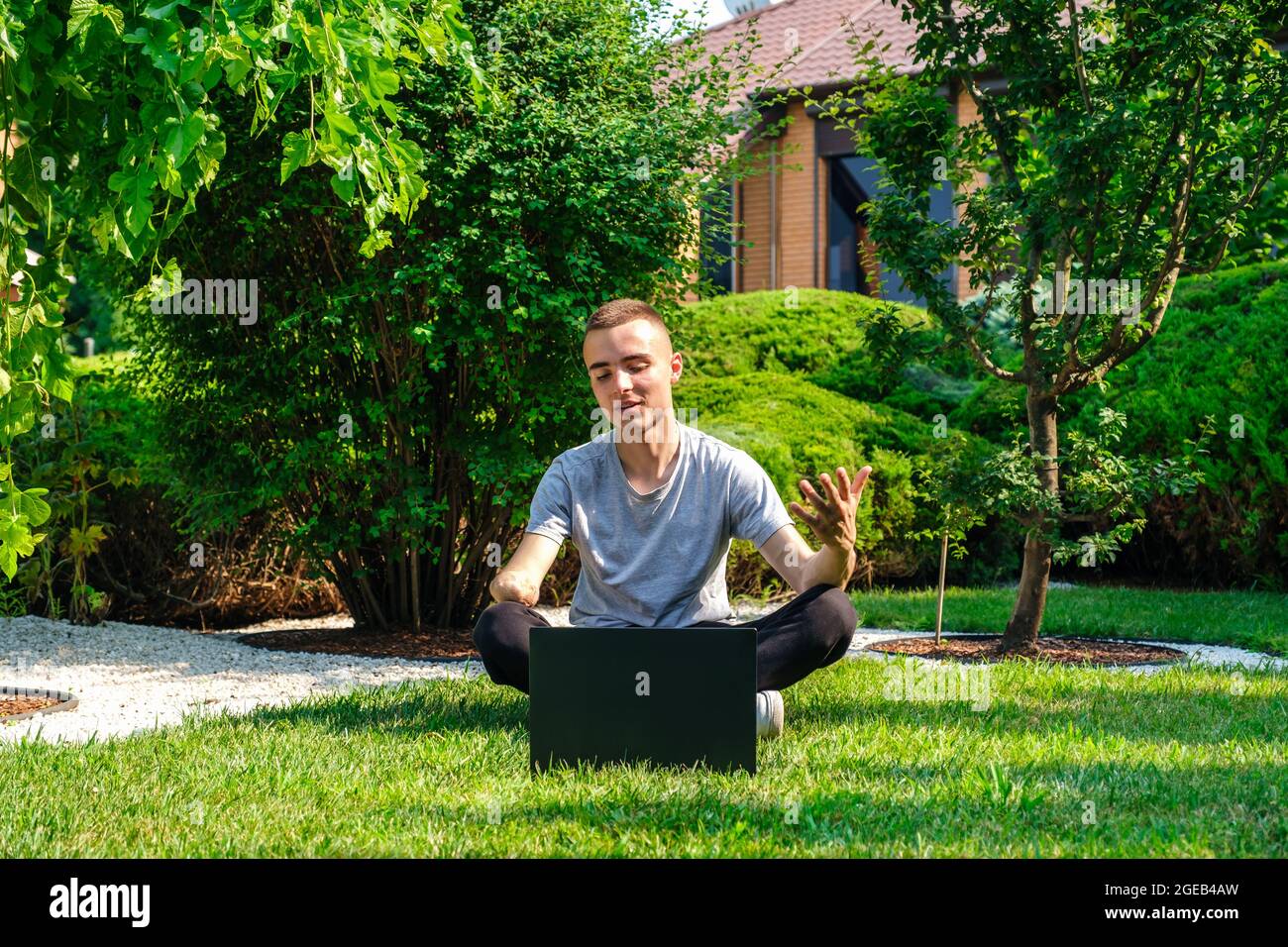 Il ragazzo con braccio amputato siede sul prato e parla con gli amici tramite social network Foto Stock