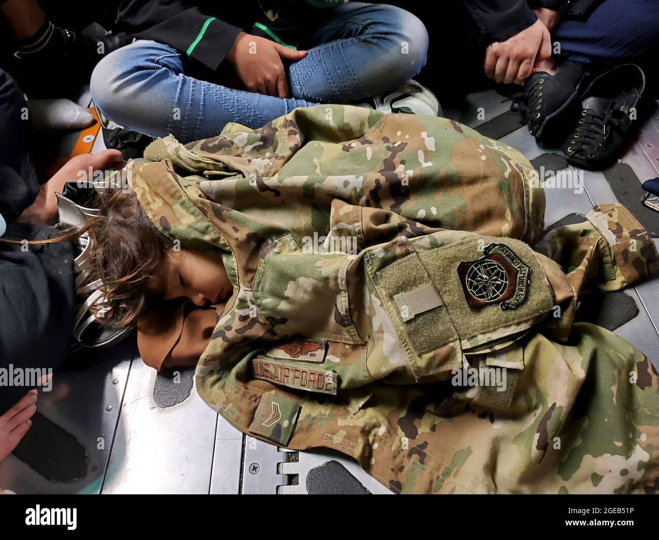 Un bambino afghano dorme sul pavimento di carico di un'aeronautica degli Stati Uniti C-17 Globemaster III, tenuto caldo dall'uniforme di Airman First Class Nicolas Baron, C-17 loadmaster, durante un volo di evacuazione da Kabul, Afghanistan, 18 agosto 2021. Operando una flotta di Air National Guard, Air Force Reserve e Active Duty C-17s, Air Mobility Command, a sostegno del Dipartimento della Difesa, ha spostato le forze in teatro per facilitare la partenza e il trasferimento sicuro dei cittadini statunitensi, dei beneficiari del visto speciale per l'immigrazione e delle popolazioni afghane vulnerabili dall'Afghanistan. (Foto gentilmente concessa dal 1° Lt. Mark Lawson, 6° ai Foto Stock