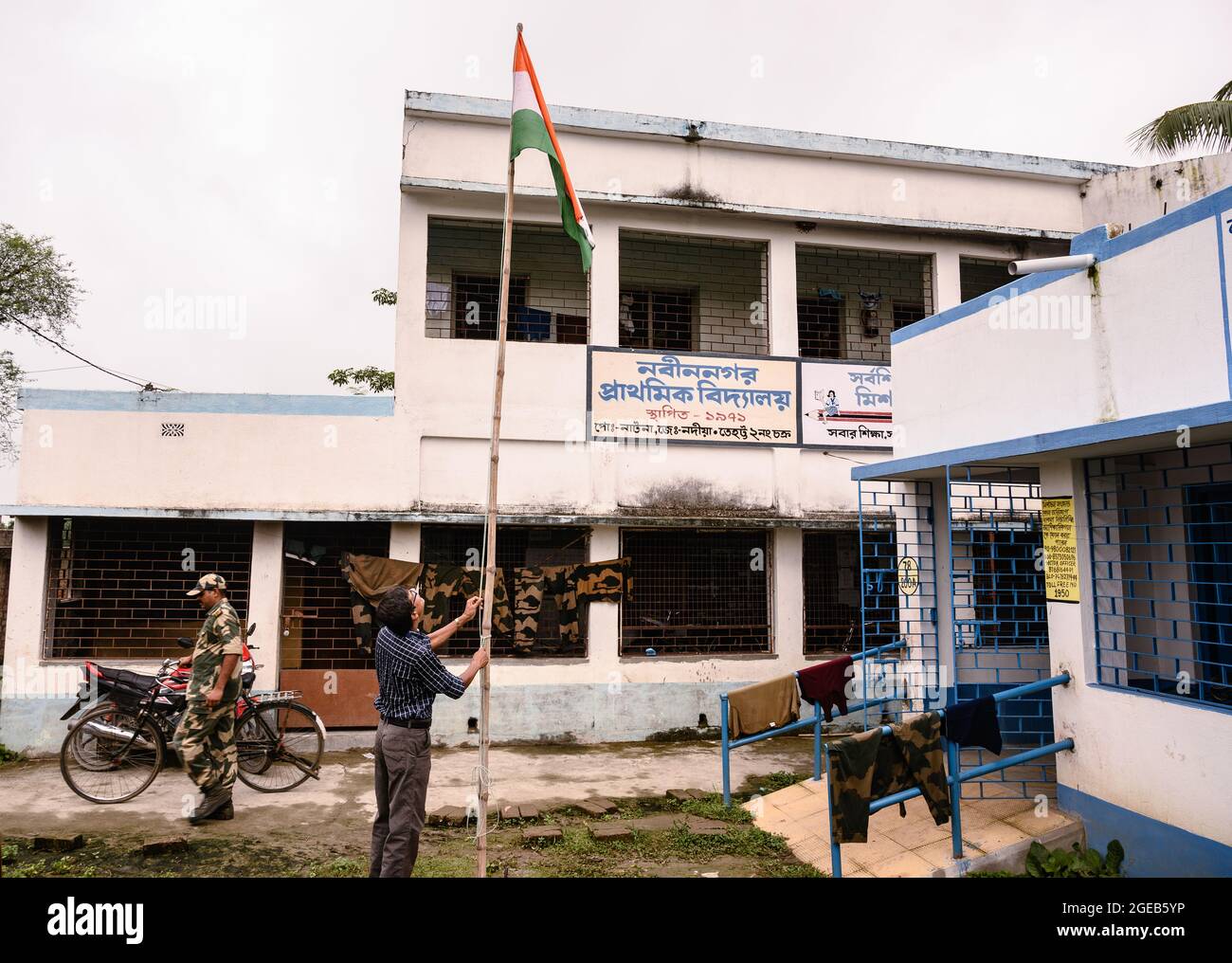 Il direttore della scuola ha issato la bandiera nazionale indiana senza studenti il giorno dell'Indipendenza seguendo gli standard fissati negli anni precedenti prima del COVID – 19. La scuola primaria rurale sul confine tra India e Bangladesh è stata un centro di quarantena per la forza di sicurezza del confine indiano (BSF), e gli studenti non hanno il permesso di entrare nella scuola. Nabin Nagar, Bengala Occidentale; India. Foto Stock