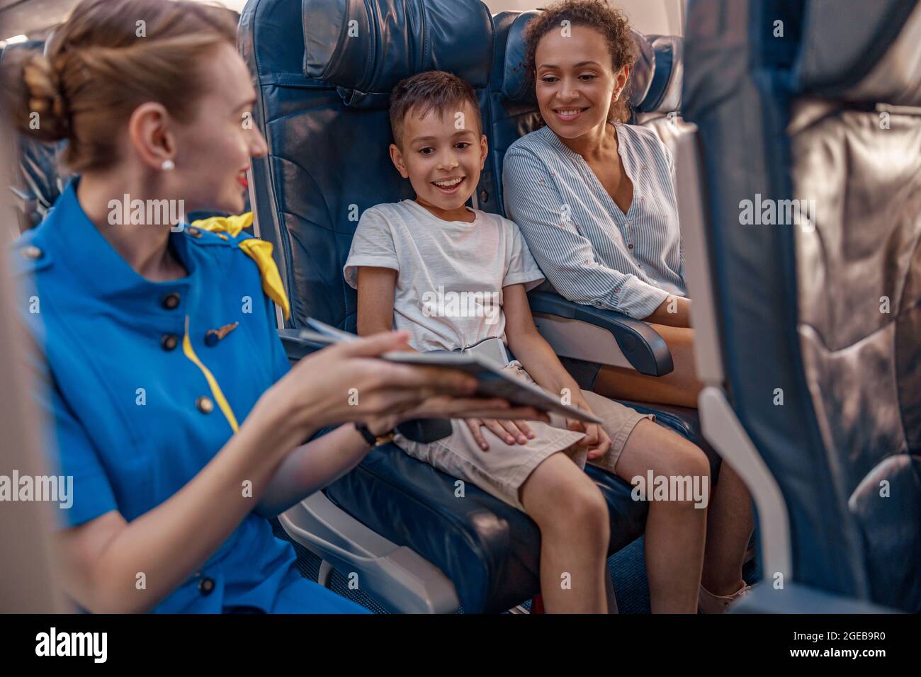 Hostess aria femminile cercando di intrattenere un bambino sull'aereo offrendo un libro da leggere. L'equipaggio di cabina fornisce il servizio alla famiglia in aereo Foto Stock