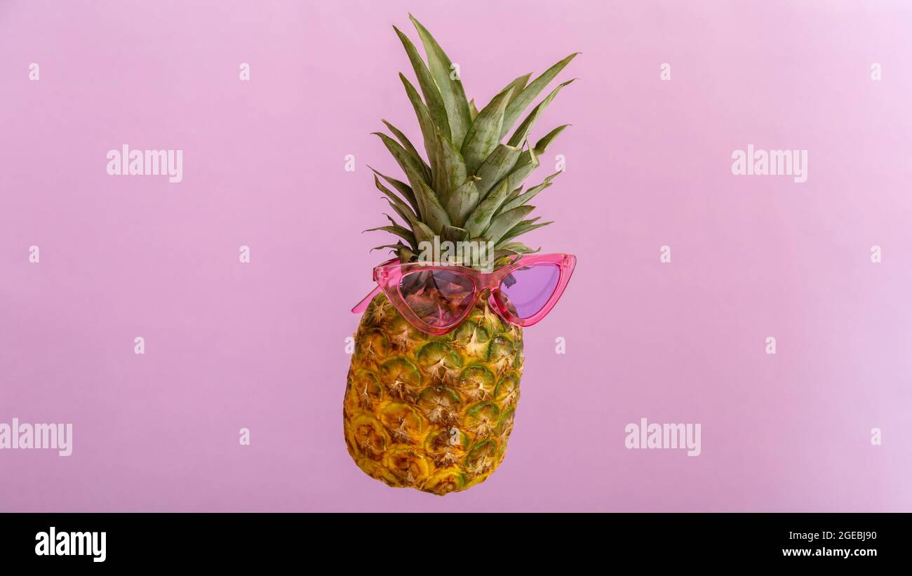 Ananas facce creative in occhiali da sole a colori su sfondo estivo di colore rosa. Tropicale frutta di ananas estate levitating in vetri rosa del sole. Estate Foto Stock