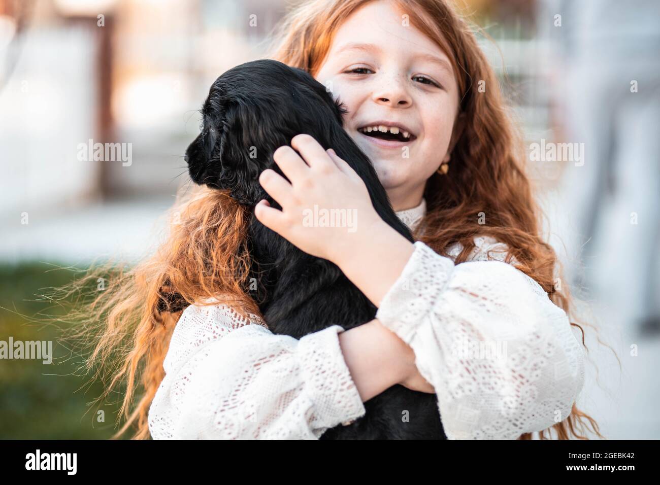 Bambina di capelli rossi abbracciando il suo nuovo amico, carino cucciolo nero Foto Stock