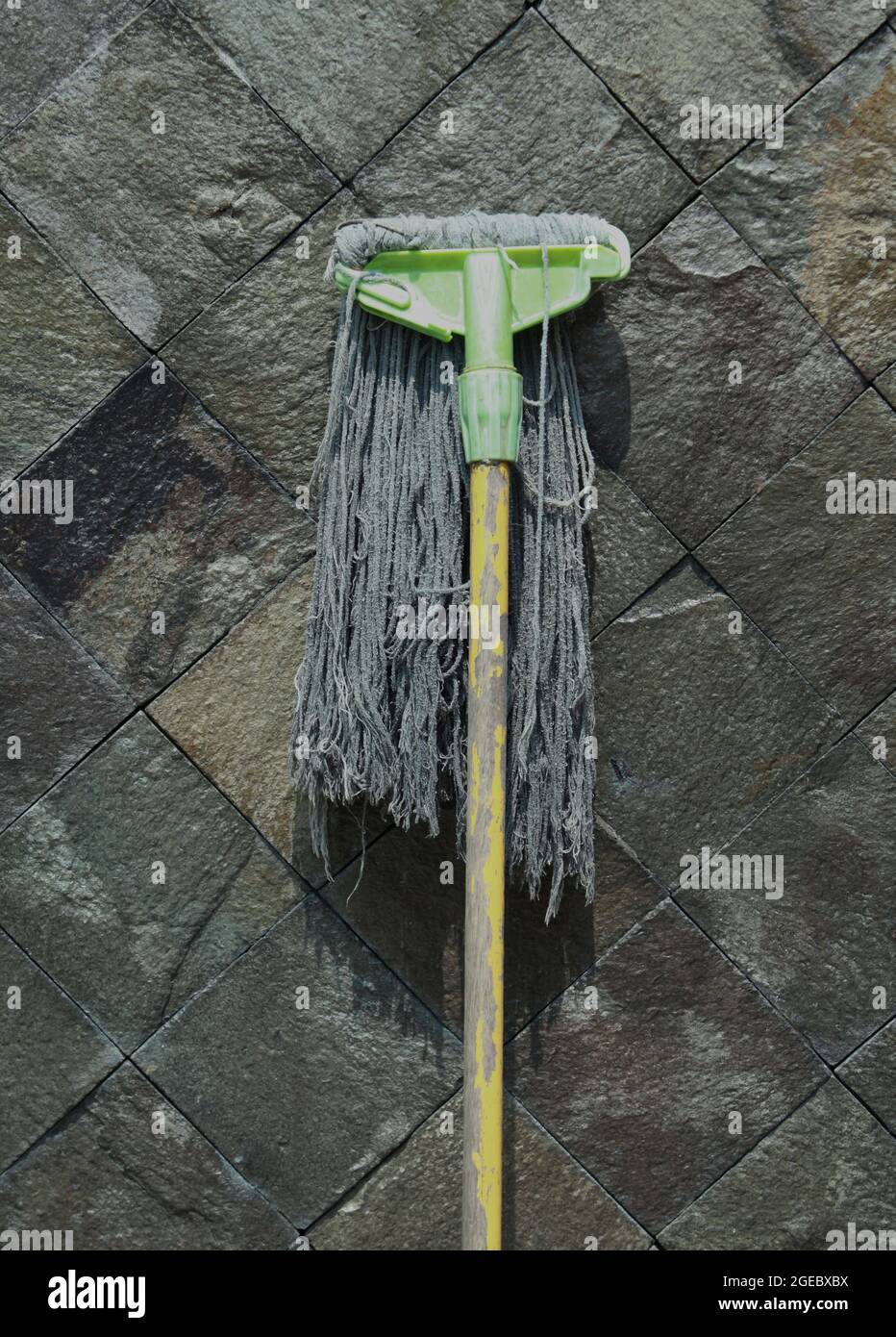 Primo piano di un mop manuale rotto su un muro di pietra Foto Stock