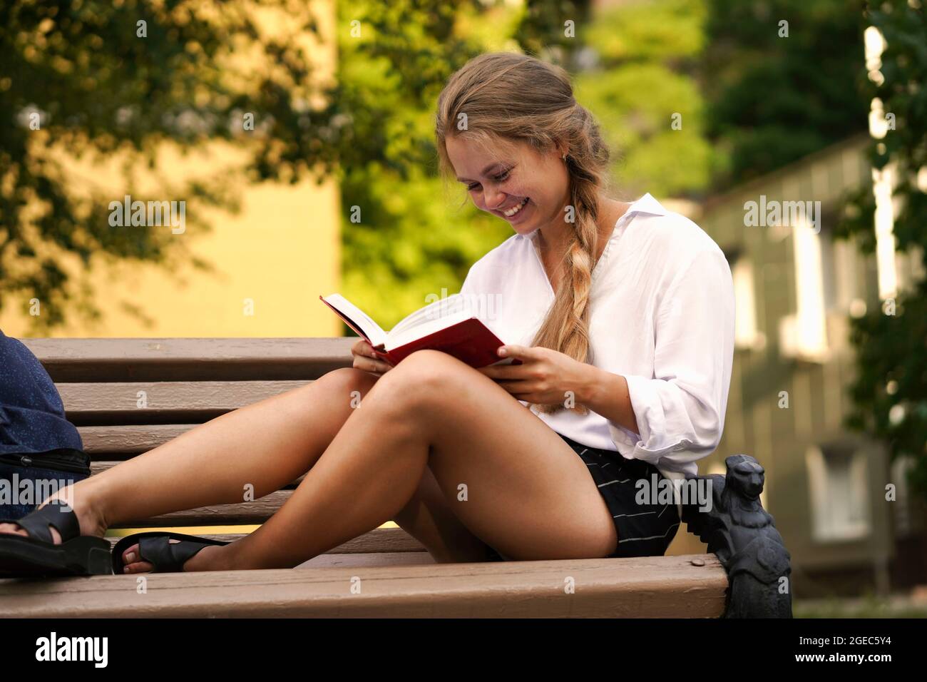 Caucasica bionda università femminile, studente universitario seduto su una panchina e la lettura di un libro. Concetto di ritorno a scuola, università, università, campus. Foto Stock