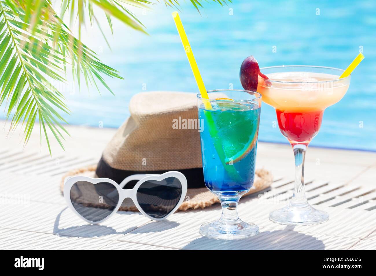 Due colorati bicchieri da cocktail, occhiali da sole e cappello al bordo della piscina Foto Stock