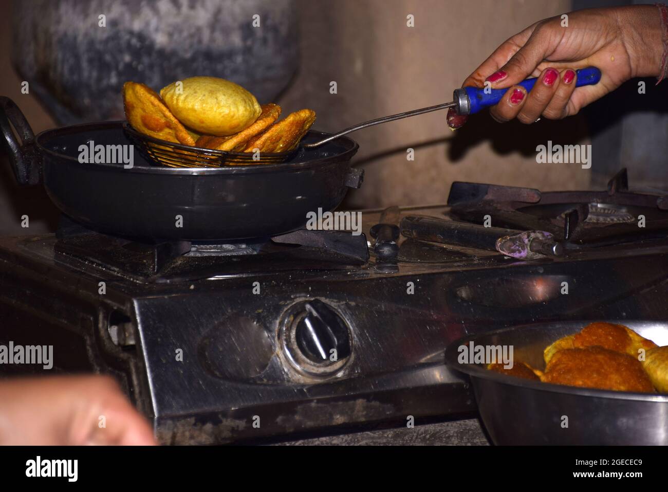 Mani di una donna che frigge poodi su stufa a gas GPL, olio bollente in padella con fondo scuro Foto Stock