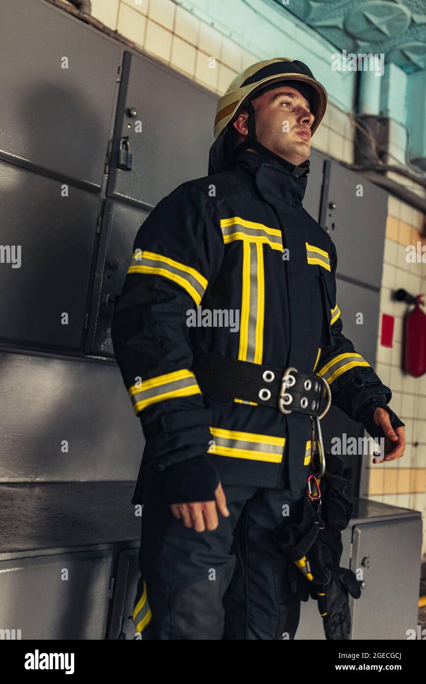 Un pompiere maschile vestito in uniforme con casco protettivo alla stazione  dei vigili del fuoco Foto stock - Alamy