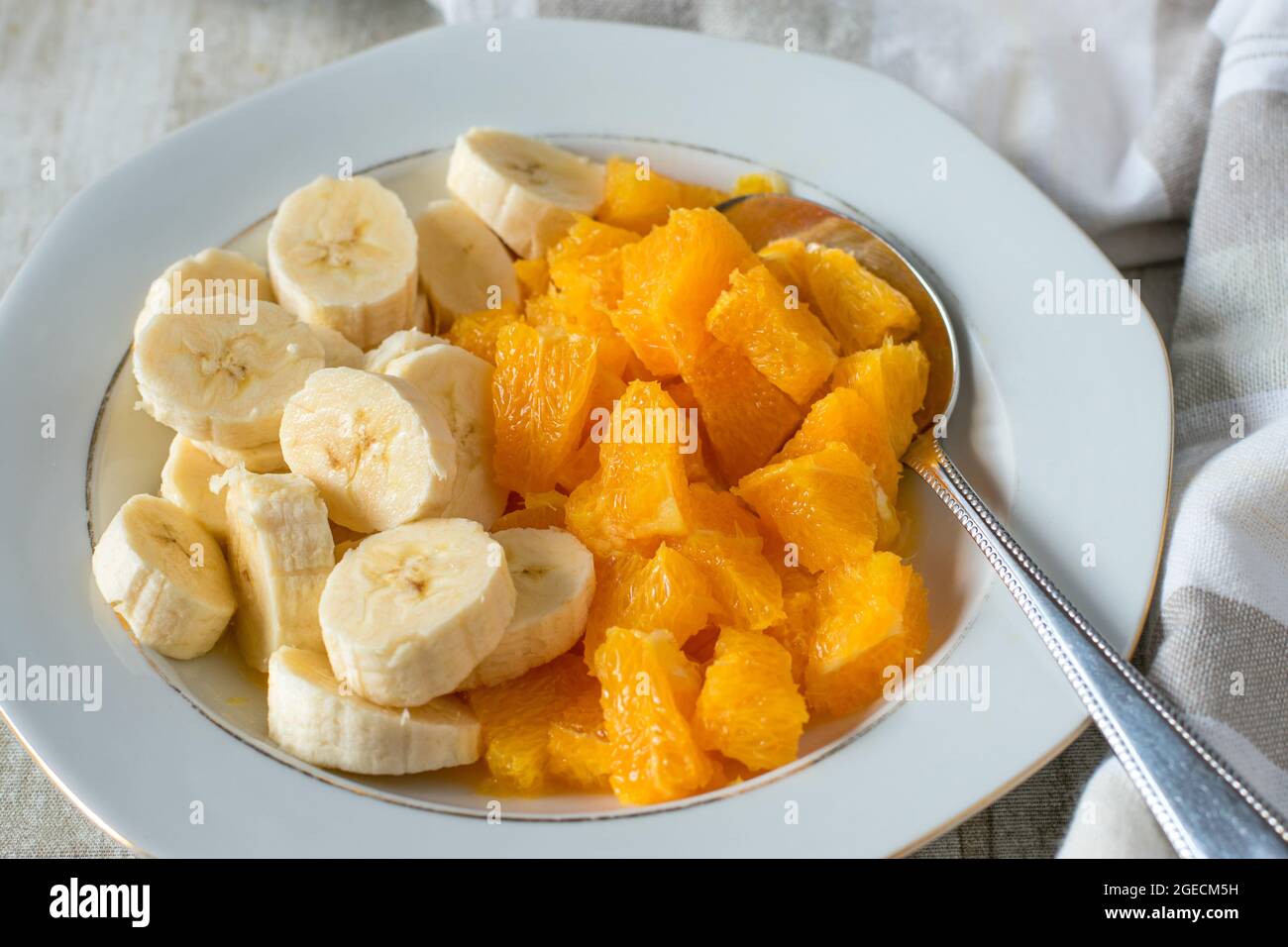 Un piatto con arance e banane tritate su sfondo chiaro del tavolo Foto Stock