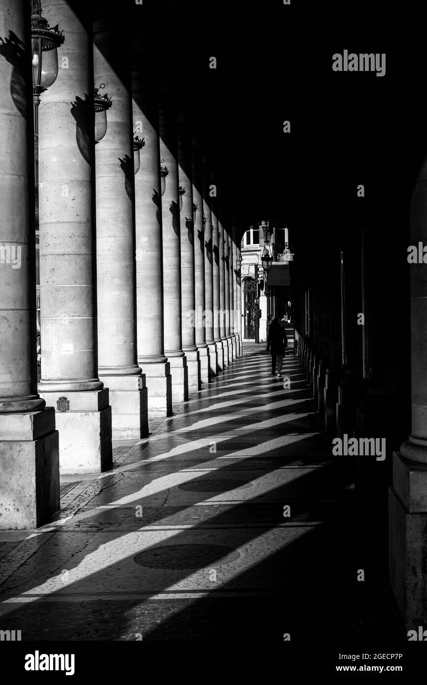 Passerella parigina in bianco e nero. Una persona non identificabile cammina nelle ombre colte da antiche colonne architettoniche. Parigi, Francia. Foto Stock