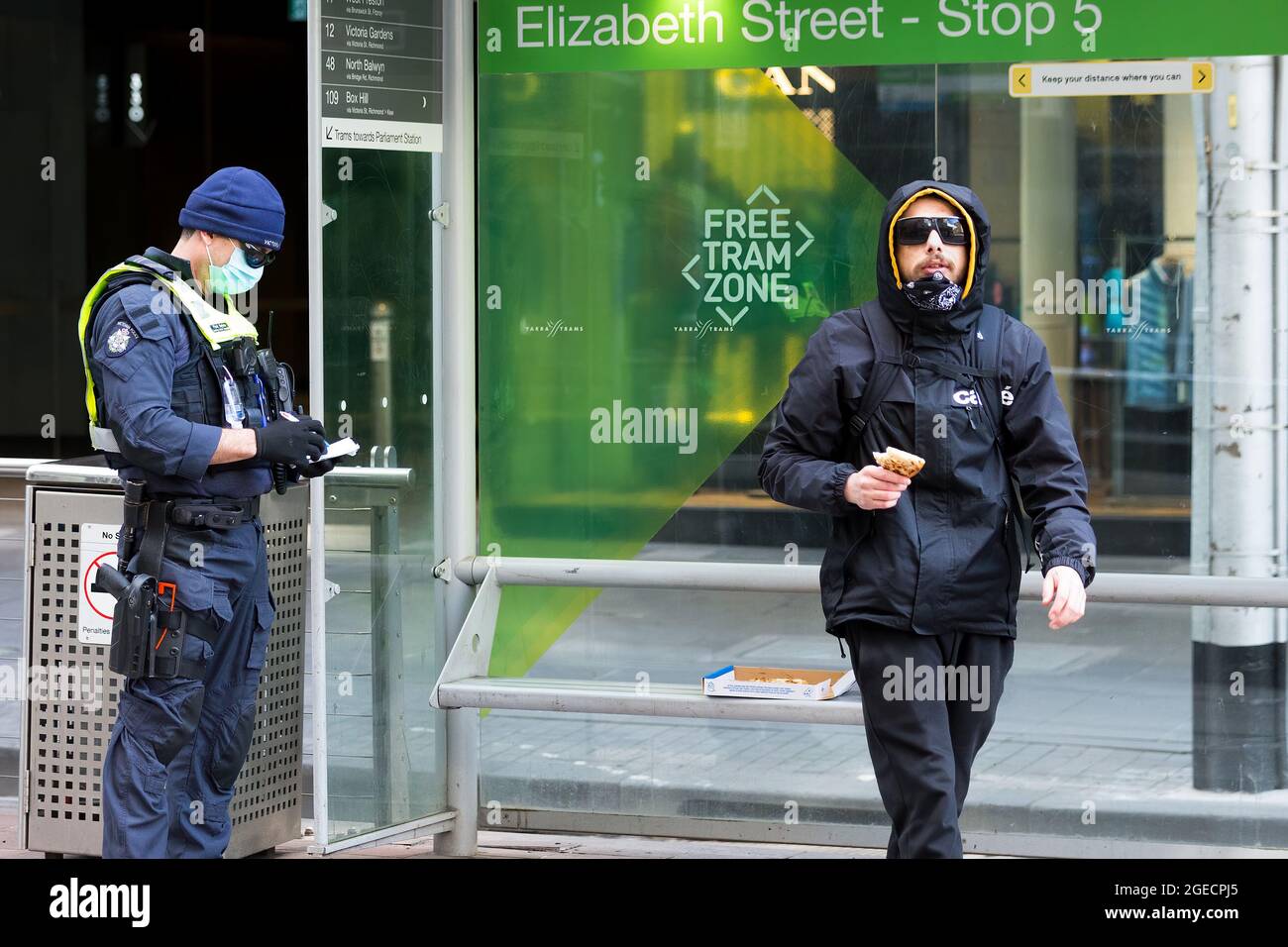 Melbourne, Australia, 9 agosto 2020. La polizia affronta un uomo in attesa di un tram per essere fuori per una ragione illegale. È stato visto per essere molto agitato ed è stato sentito abusare della polizia così come il fotografo che scattava questa foto. Egli sosteneva che era un australiano indigeno, e che scattare la sua foto era illegale. La polizia lo multò in seguito per aver infranguto le restrizioni durante il COVID-19 a Melbourne, Australia. Mentre le restrizioni della fase 4 continuano a strangolare la città di Melbourne, altri 394 nuovi casi di Coronavirus sono stati scoperti durante la notte insieme ai 17 morti, il peccato più letale di Victoria Foto Stock