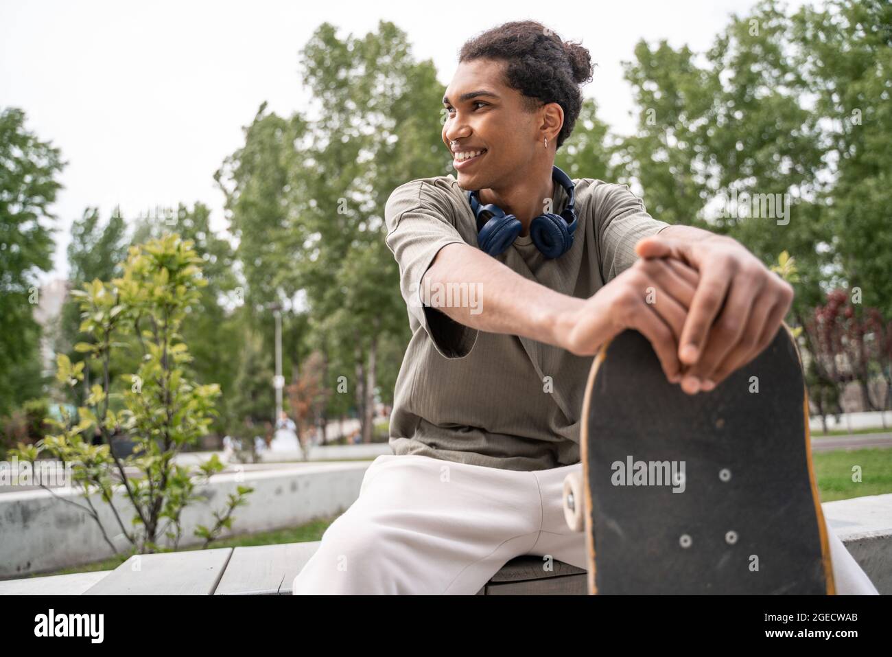 giovane e gioioso pattinatore afroamericano che guarda via mentre si siede nello skate park Foto Stock