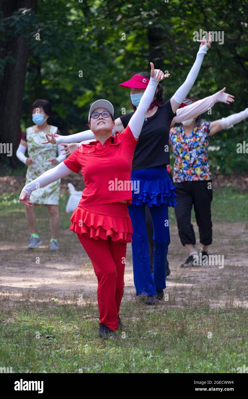 Una donna in rosso in una lezione di danza in un parco a Queens, New York. Foto Stock