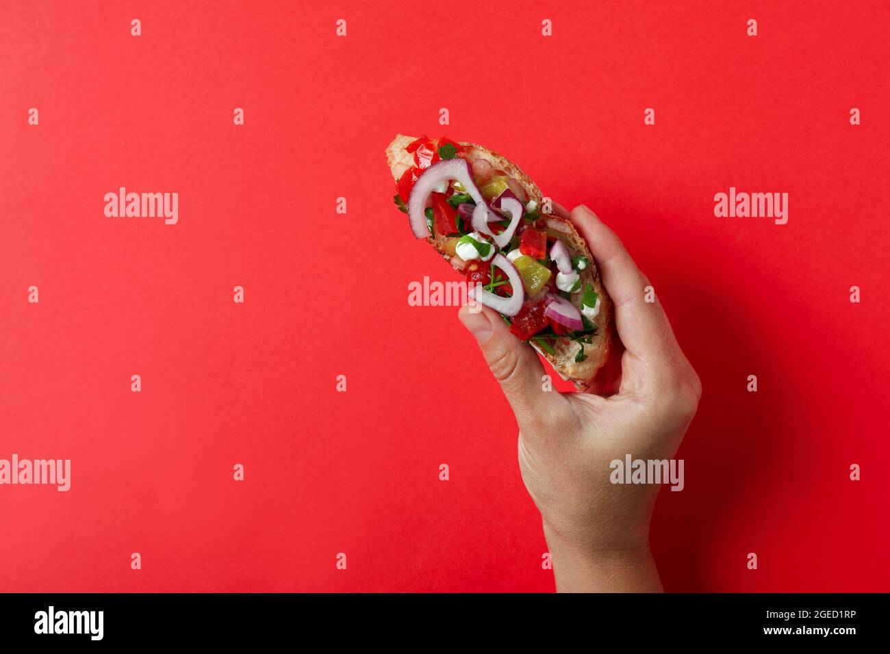 La mano femmina tiene la bruschetta su sfondo rosso Foto Stock
